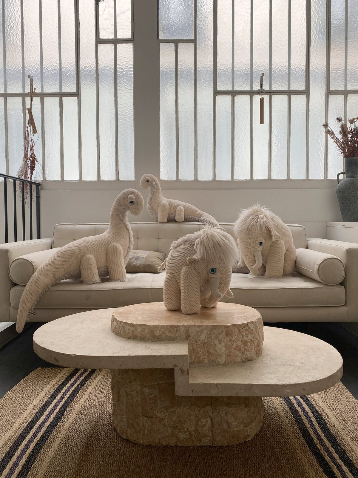 Dinosaur and mammoth plushes lounging on a sofa in a bright living room