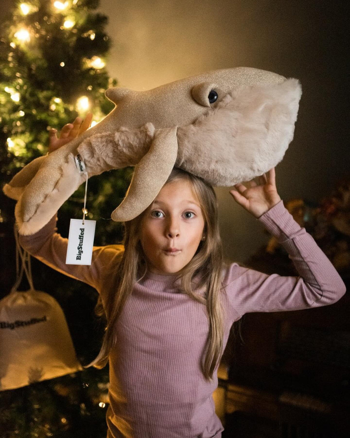 Surprised girl with a big whale plush on her head next to the Christmas tree